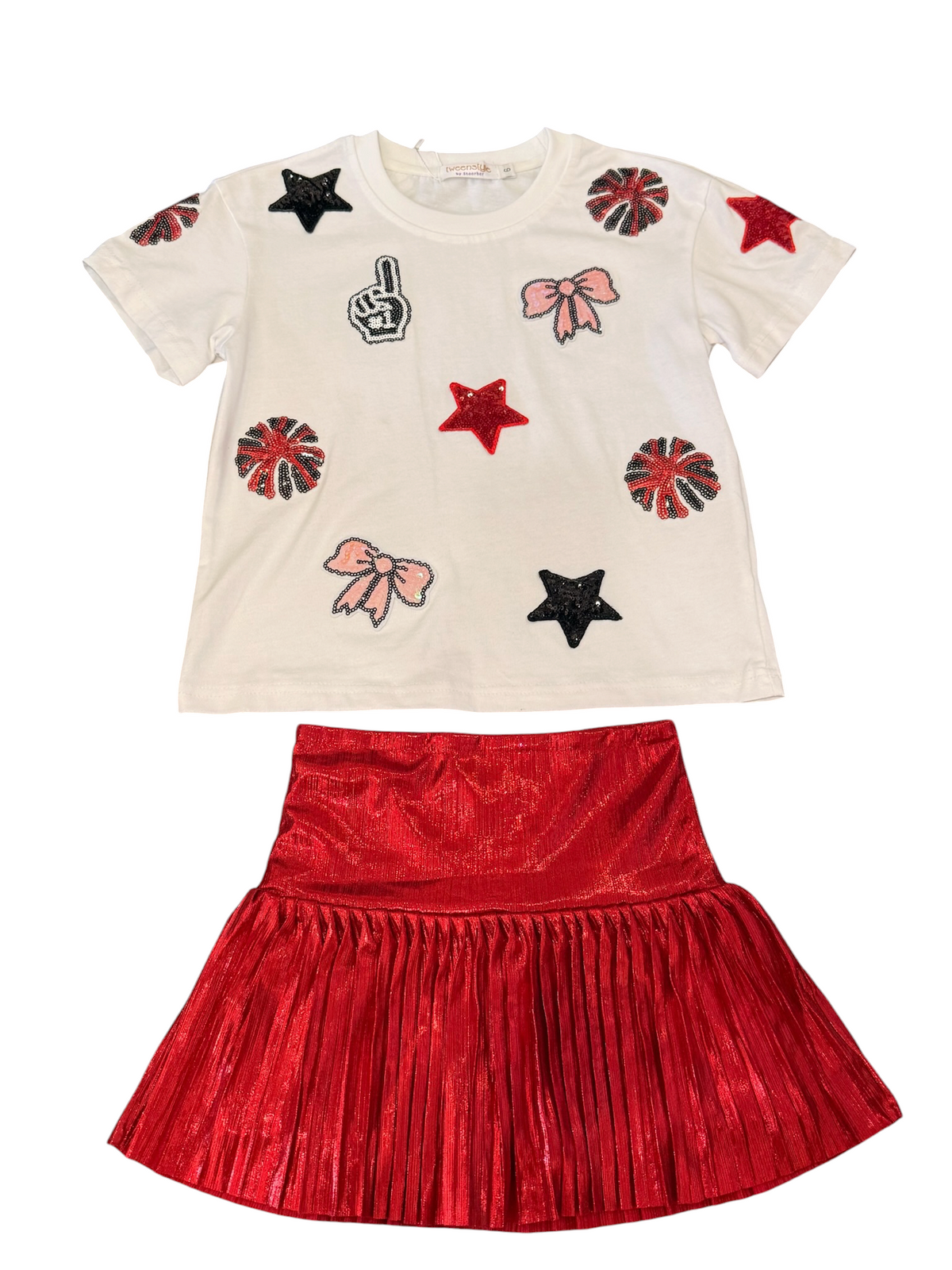 A children's two-piece outfit featuring a cream short-sleeve top with red, black, and pink cheerleader-style patches, paired with a shiny red pleated skirt, shown on a plain white background.