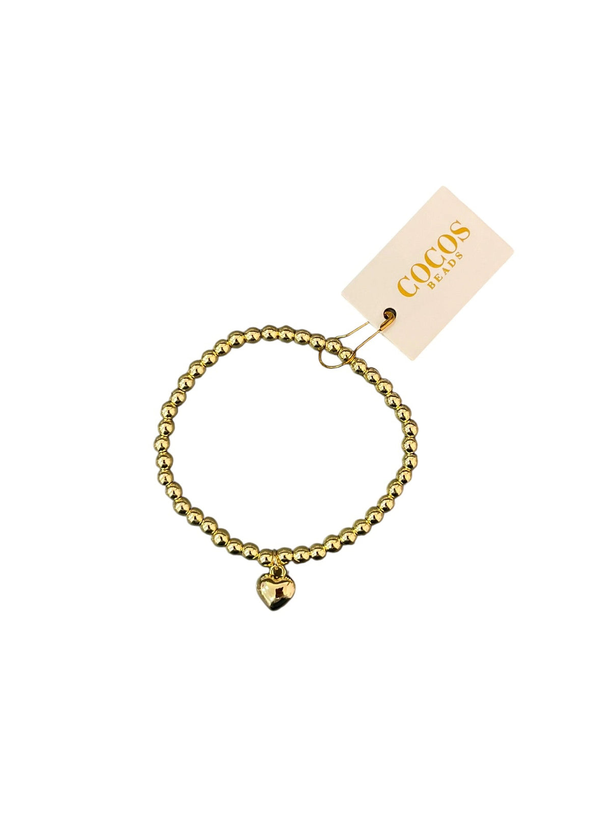 A gold beaded stretch bracelet with a small heart charm, shown with its branded paper tag on a plain white background.