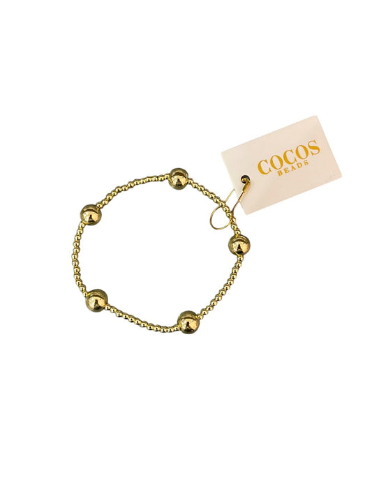 A gold beaded bracelet with five evenly spaced, polished spherical beads, shown with a cream-colored brand tag that reads 'COCOS BEADS'.