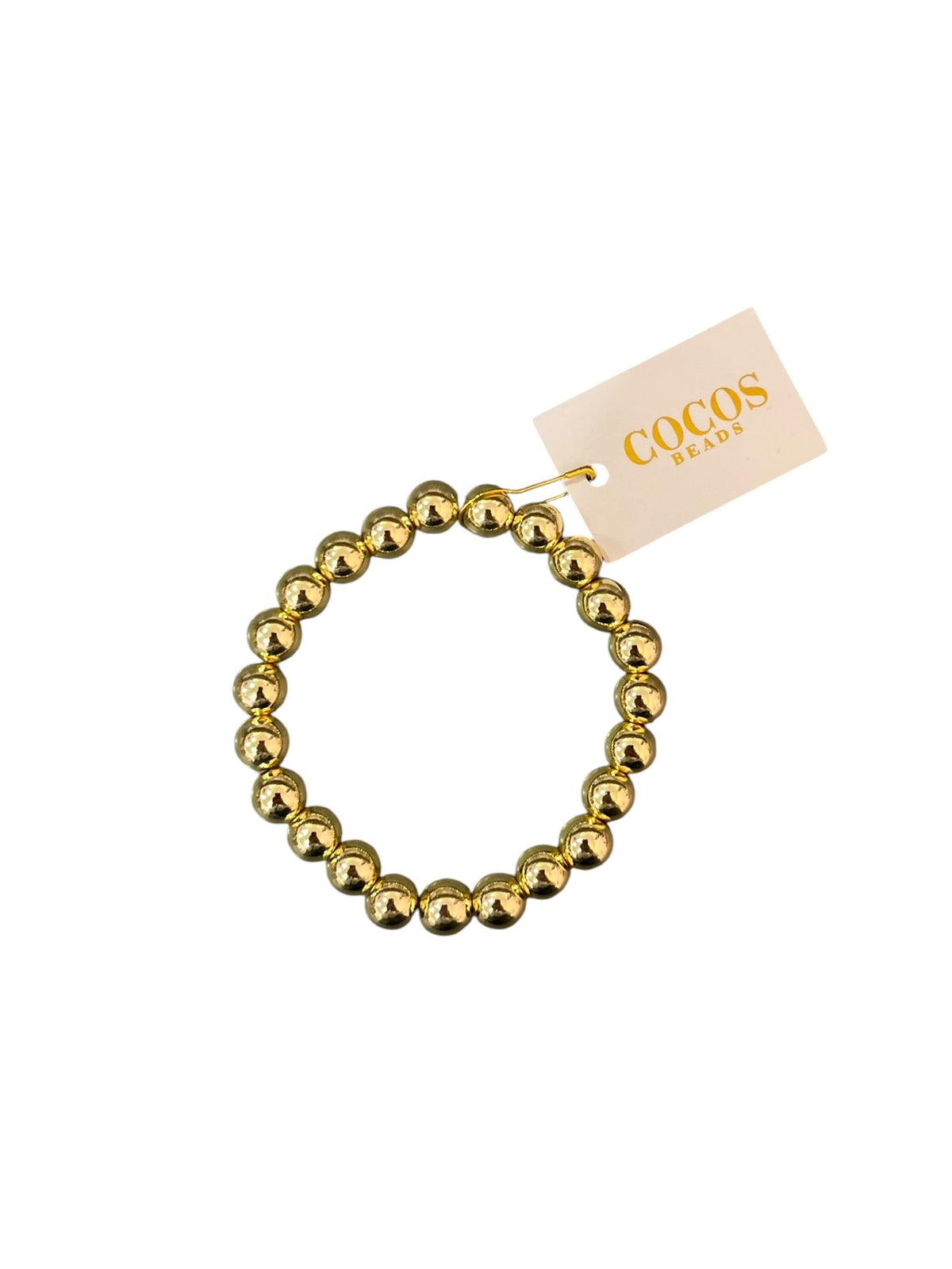 A gold beaded stretch bracelet with a small paper tag attached, featuring the brand name 'COCOS BEADS' in gold lettering, set against a plain white background.