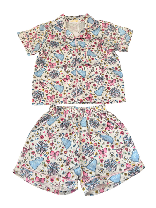 A two-piece loungewear set featuring a short-sleeve button-up shirt and matching shorts, both printed with a colorful pattern of pink bows, blue megaphones, and small flowers on a cream background.